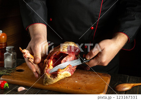 Cooking duck on the kitchen table. Cozy low key kitchen setting while cutting the bird carcass with a knife. Chef in black uniform cutting raw duck. 123167331