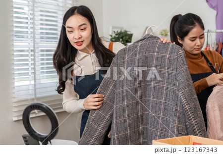 Couple selling clothes online, inspecting stylish plaid jacket and preparing other items in their cozy workspace Couple selling clothes online, inspecting stylish plaid jacket and preparing other items in their cozy workspace 123167343