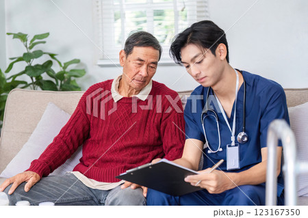 Nurse documenting patient information while elderly man listens attentively during a home visit 123167350
