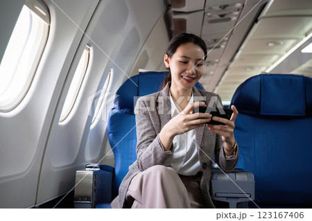 Young Asian woman checks business news on mobile phone, sitting near window in first class on airplane during flight, travel and business concept 123167406