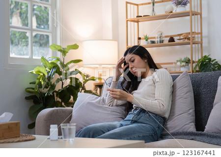 Young Woman Sitting on Couch Taking Medicine While Feeling Sick at Home in a Cozy Living Room Setting 123167441