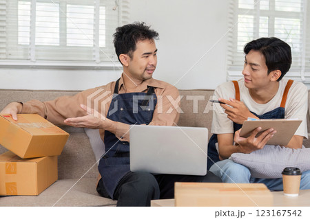 LGBT couple discussing online sales strategy, reviewing packaging while seated on a couch at home LGBT couple discussing online sales strategy, reviewing packaging while seated on a couch at home 123167542