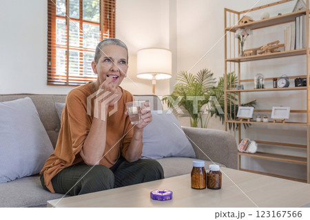 Elderly woman Taking Medicine with a Glass of Water in a Cozy Home Setting for Health and Wellness Concept 123167566