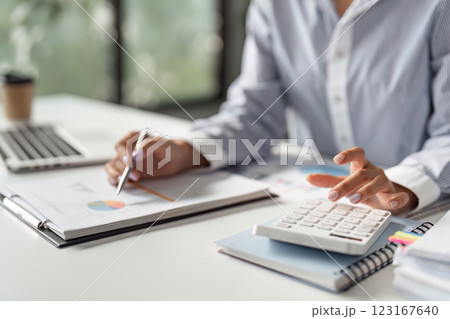 Finance worker calculating data with a calculator and reviewing reports in a modern office. Finance worker calculating data with a calculator and reviewing reports in a modern office. 123167640