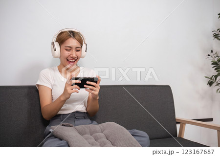 Young Woman Relaxing in Modern Living Room with Headphones and Smartphone, Enjoying Leisure Time on Comfortable Sofa Young Woman Relaxing in Modern Living Room with Headphones and Smartphone, Enjoying Leisure Time on Comfortable Sofa 123167687