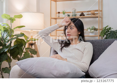 Young Woman Feeling Unwell Sitting on Sofa at Home, Holding Forehead, Looking Concerned and Tired Young Woman Feeling Unwell Sitting on Sofa at Home, Holding Forehead, Looking Concerned and Tired 123167775