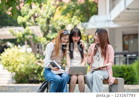 Happy Asian teenage female college students tutor together in the garden outside the university classroom. Female students happily help each other with their homework. 123167793