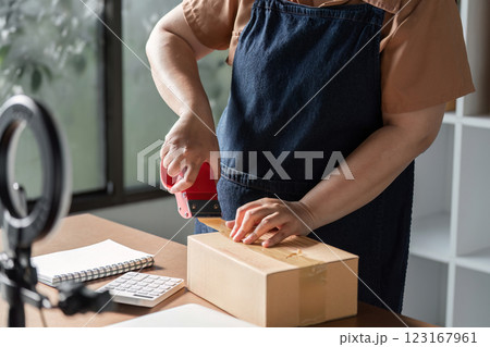 Young woman entrepreneur packaging items for livestream sales in a modern home office setup 123167961