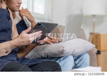 Couple reviewing plans on a tablet and laptop while seated comfortably in their modern living room 123168049