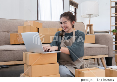 Young woman, small business owner selling products online, accepting online product orders via laptop, sits in a room with boxes of products. 123168063