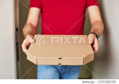 delivery man in red t-shirt giving food order and holding pizza box at home, close-up 123168192