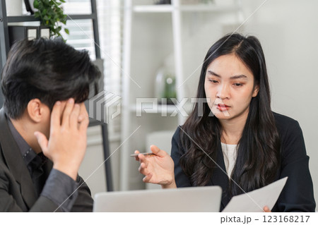 Professional woman discussing project challenges with a stressed male colleague in a modern office setting. 123168217