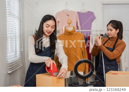 Two diverse retail workers packing boxes and preparing shipments in a clothing store. 123168249