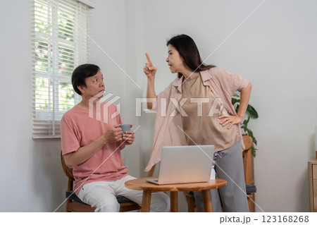 Frustrated woman scolding man while he sits at a table with a laptop and mug. Frustrated woman scolding man while he sits at a table with a laptop and mug. 123168268