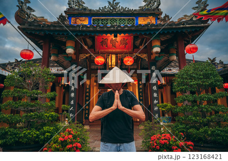 male tourist in a Vietnamese Non La hat prays at temple on a Buddhist pagoda in Hoi An in Vietnam in Asia 123168421