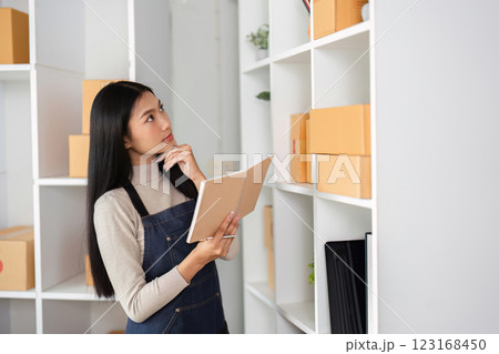 E-commerce businesswoman contemplating inventory while holding a notebook in a modern office. E-commerce businesswoman contemplating inventory while holding a notebook in a modern office. 123168450