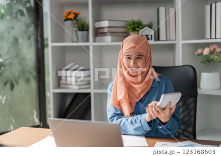 Muslim woman using calculator and laptop while analyzing financial data in a modern workspace. 123168603