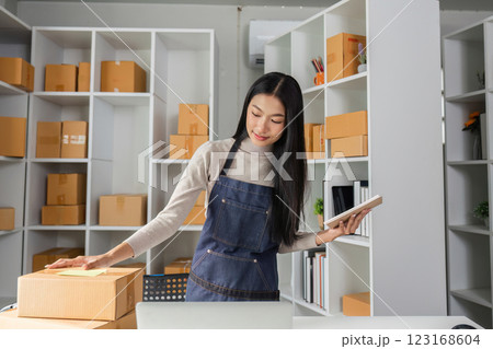 Young woman managing inventory in a modern workspace, organizing packages and using a notebook. 123168604