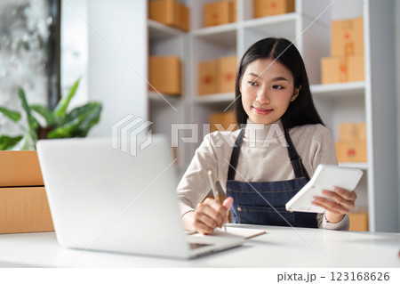 Thoughtful Asian woman reviewing e-commerce data on a tablet in a modern workspace. Thoughtful Asian woman reviewing e-commerce data on a tablet in a modern workspace. 123168626