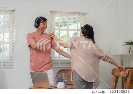 Joyful older couple dancing together with headphones in their home. Joyful older couple dancing together with headphones in their home. 123168628