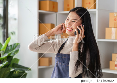 Happy young woman in apron talking on the phone while managing inventory in a modern workspace. 123168682