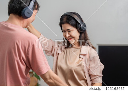 Mature couple joyfully dancing at home with headphones, enjoying music. 123168685