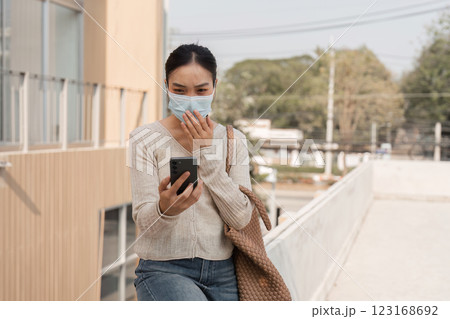 Diverse woman wearing a mask while surprised by smartphone notification outdoors. Diverse woman wearing a mask while surprised by smartphone notification outdoors. 123168692