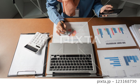 Muslim woman reviewing budget pie chart while holding smartphone at her desk. Muslim woman reviewing budget pie chart while holding smartphone at her desk. 123168730