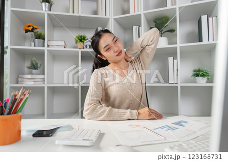 Woman stretching neck while sitting at her desk, experiencing office syndrome symptoms. 123168731