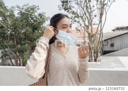 Young woman removing her mask while smiling outdoors in a public space. Young woman removing her mask while smiling outdoors in a public space. 123168732