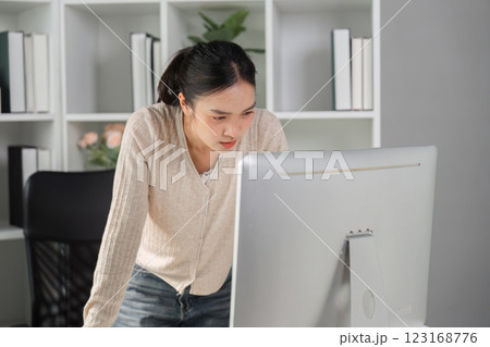 Woman leaning on desk while working intently on a computer in an office environment. 123168776