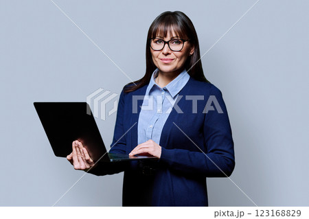 Middle aged businesswoman holding laptop looking at camera on grey studio background Middle aged businesswoman holding laptop looking at camera on grey studio background 123168829