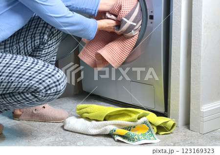 Woman in pajamas puts dirty towels and bedding into open washing machine. Cleaning and putting apartment in order. Modern interior and lifestyle.  123169323