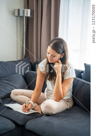 Young woman siting on the sofa and writing her personal diary, writing down thoughts, dreams and plans as part of psychotherapy after working with neurocoaching Young woman siting on the sofa and writing her personal diary, writing down thoughts, dreams and plans as part of psychotherapy after working with neurocoaching 123170089