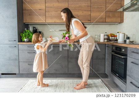 Little girl giving bouquet of flowers and drawing to her mum on the home kitchen. Mothers day, birthday or International Women's Day 8 march concept 123170209