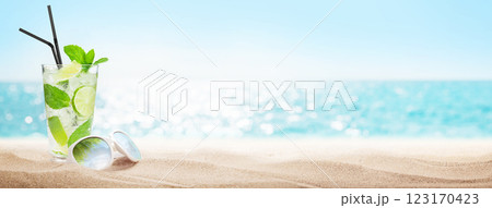 A refreshing mojito cocktail with fresh mint and lime, placed next to stylish sunglasses on beach 123170423