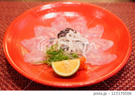 赤い皿に並べられた3年トラフグのてっさ一人前と上に乗せられたてっぴ 赤い皿に並べられた3年トラフグのてっさ一人前と上に乗せられたてっぴ 123170506