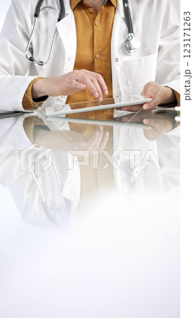 Unknown male doctor wearing a stethoscope, yellow shirt under a lab coat, is using digital tablet in modern healthcare setting, interacting with patient data, vertical portrait. Medicine concept Unknown male doctor wearing a stethoscope, yellow shirt under a lab coat, is using digital tablet in modern healthcare setting, interacting with patient data, vertical portrait. Medicine concept 123171263