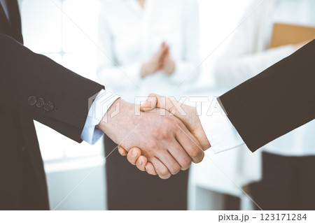 Businessman and woman shaking hands with colleagues at the background. Handshake at meeting in office. Concept of success in business Businessman and woman shaking hands with colleagues at the background. Handshake at meeting in office. Concept of success in business 123171284