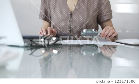 Businesswoman accountant in brawn dotted blouse reviewing financial reports with magnifying glass and calculator, conducting audit and analyzing data in office. Taxes, audit in business Businesswoman accountant in brawn dotted blouse reviewing financial reports with magnifying glass and calculator, conducting audit and analyzing data in office. Taxes, audit in business 123171300