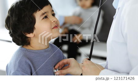 Doctor-woman examining a child patient by stethoscope. Cute arab boy and his brother at physician appointment. Medicine concept 123171426