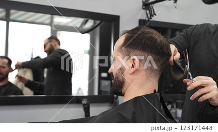 Skilled barber trimming client's hair using professional scissors, creating contemporary hairstyle in modern barbershop setting with precise, professional technique. Skilled barber trimming client's hair using professional scissors, creating contemporary hairstyle in modern barbershop setting with precise, professional technique. 123171448