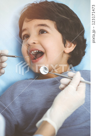 Cute arab boy sitting at dental chair with open mouth during oral checking up with doctor. Visiting sunny dentist office 123171473