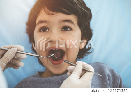 Cute arab boy sitting at dental chair with open mouth during oral checking up with doctor. Visiting sunny dentist office Cute arab boy sitting at dental chair with open mouth during oral checking up with doctor. Visiting sunny dentist office 123171522