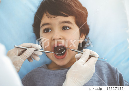 Cute arab boy sitting at dental chair with open mouth during oral checking up with doctor. Visiting sunny dentist office Cute arab boy sitting at dental chair with open mouth during oral checking up with doctor. Visiting sunny dentist office 123171524