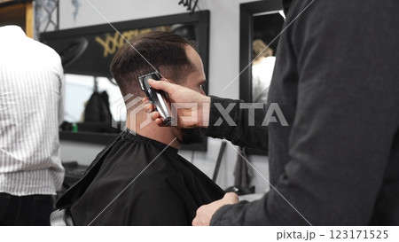 Skilled barber trimming client's hair using electric razor, creating contemporary hairstyle in modern barbershop setting with precise, professional technique Skilled barber trimming client's hair using electric razor, creating contemporary hairstyle in modern barbershop setting with precise, professional technique 123171525