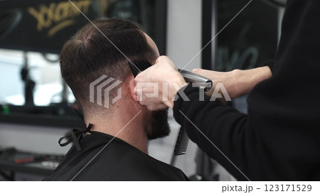 Skilled barber trimming client's hair using electric razor, creating contemporary hairstyle in modern barbershop setting with precise, professional technique Skilled barber trimming client's hair using electric razor, creating contemporary hairstyle in modern barbershop setting with precise, professional technique 123171529