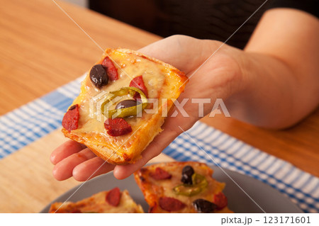 Caucasian white person holding pizza pieces on bamboo cutting board and gray plate on blue napkin Caucasian white person holding pizza pieces on bamboo cutting board and gray plate on blue napkin 123171601