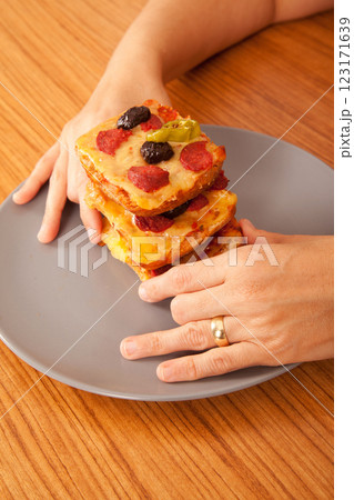 Caucasian white person holding delicious pizza slices in grey plate on wooden table Caucasian white person holding delicious pizza slices in grey plate on wooden table 123171639