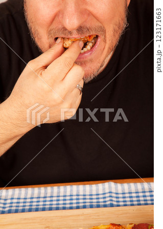 Bearded caucasian white mature male in black t-shirt eating delicious pizza slices on bamboo cutting board on table 123171663